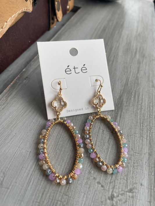 Pair of multi-color beaded earrings on a 'été' branded card on a gray surface